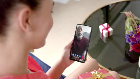 biracial woman holding smartphone with african american man with gift on screen with gift on desk