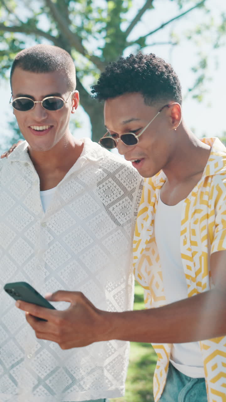 Two Young Men Laughing and Looking at Smartphone in Park