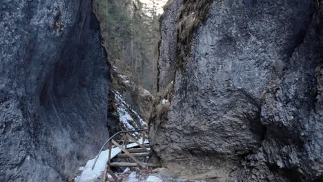 Fliegen-Sie-Im-Winter-An-Steilen-Felsbergen-Mit-Einer-Holzbrücke-Davon