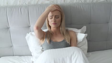 women sitting on bed holding her head  she has a painful headache