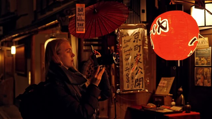 A young woman captures the enchanting nighttime atmosphere of Kyoto’s streets with her camera.