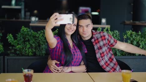 loving couple in a playful mood are taking a selfie at the table in the cafe on the background of a modern interior