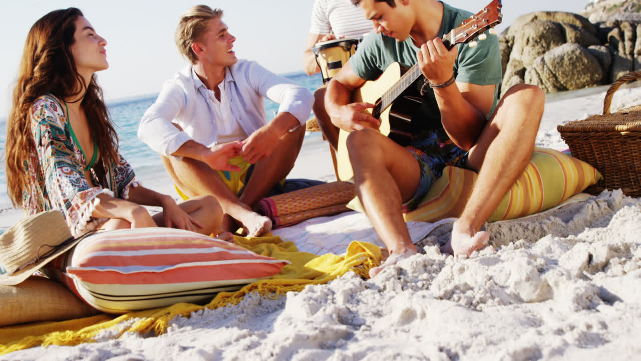 hombre tocando la guitarra para amigos sentado en la playa 4k