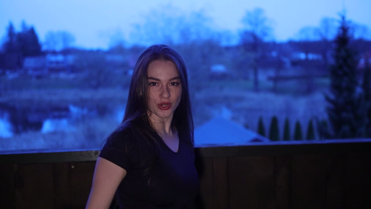 Stunning and energetic young Caucasian female dancer singing and performing on a balcony in the evening in slow motion