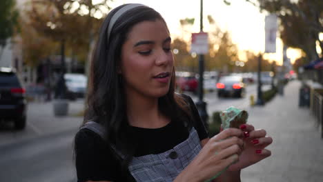 a cute young woman laughing and eating a messy ice cream cone dessert on a city street in slow motion