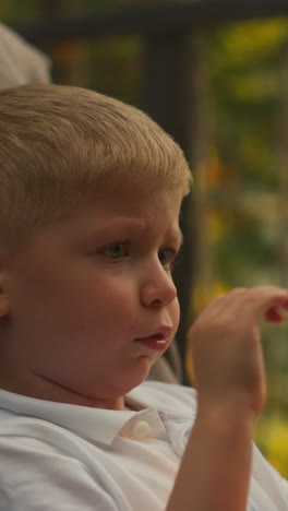 amazed boy glances at contemporary smartphone enjoying tranquil nature. thoughtful child watches cartoons on terrace admiring view of dense woodland at sunrise