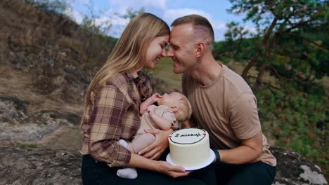 happy new parents celebrate two month of their newborn son. couple hold a cake and look at their baby with love.