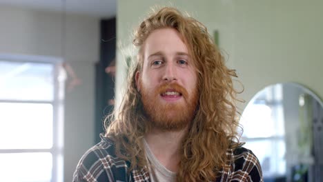 retrato de un hombre caucásico feliz con cabello rojo largo y barba sonriendo en la peluquería, en cámara lenta.