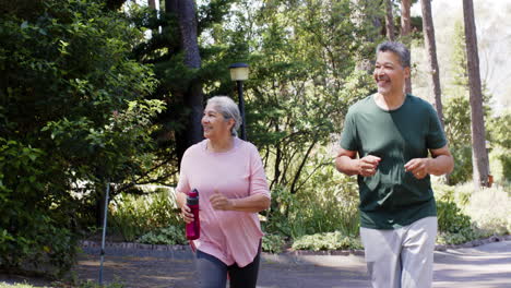 Happy-diverse-senior-couple-running-and-holding-water-bottle-in-sunny-outdoors