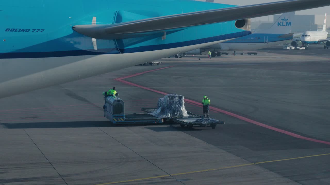 Static shot of airport workers transferring luggage across machines on the runway