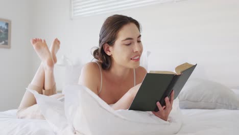 Happy-caucasian-woman-relaxing,-lying-in-bed-and-reading-book