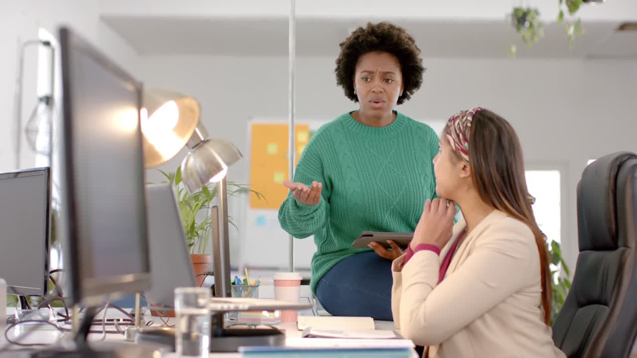 Diverse business female colleagues in discussion using laptop in casual office meeting, slow motion