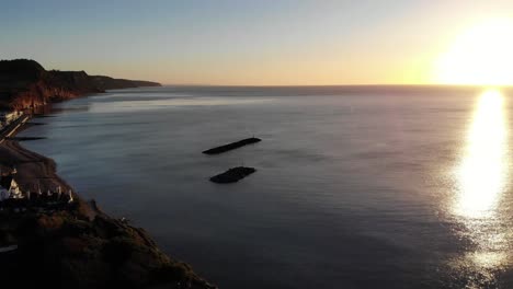 aerial rising of golden yellow morning sunrise on horizon of english channel with offshore rock breakwaters off sidmouth coastline