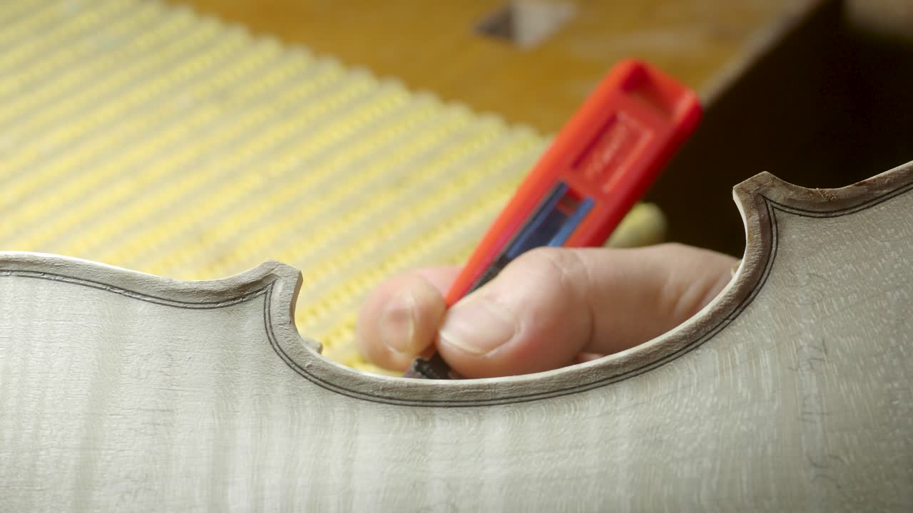 macro primer plano de artesano luthier fabricante de trabajo en nuevo clásico hecho a mano violín crudo borde liso en la cintura y raspado púrpura en el banco de trabajo del taller en cremona italia video 4k