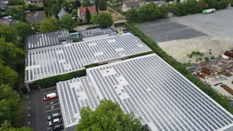 beautiful aerial of a sustainable industrial building with photovoltaic solar panels covering the rooftop and electric vehicles being charged on the company's parking lot