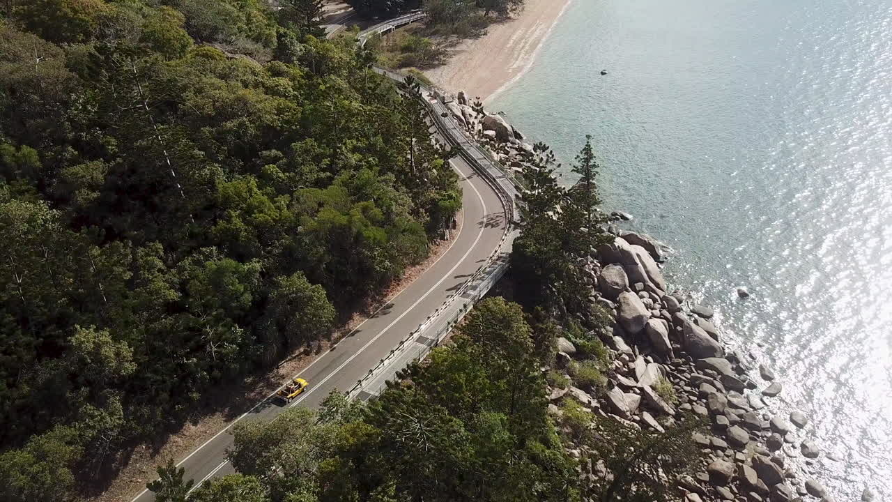 vista aérea de un buggy de playa clásico descapotable abierto conduciendo a lo largo de la carretera costera del acantilado junto al sol reflejándose en aguas tropicales cristalinas