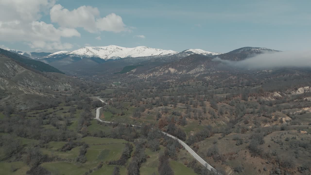 una toma de drone de montañas forestales con nieve, clima cálido, pequeño pueblo, volando sobre una colina de niebla, video 4k, naturaleza invernal europea, nubes blancas panorámicas, hermoso paisaje