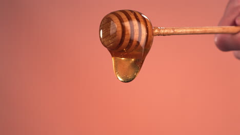 super slow motion cu honey pouring from honey stick against bright background