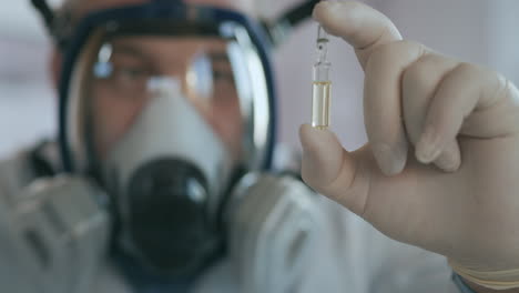 A-scientist-doctor-at-a-pharmaceutical-company-developing-a-drug-in-a-laboratory-in-a-glass-respirator-screen-holds-a-new-medicine-in-his-hands-a-white-amulet-with-a-vaccine-against-the-virus.-High-quality-4k-footage