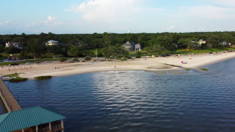 Pulling-Back-Drone-Shot-of-Pier-with-People-Walking-on-a-Beach-on-a-Clear-Sunny-Day-in-Mississippi