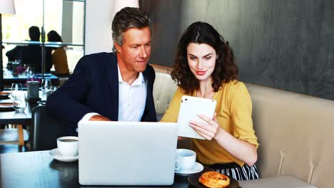 Businessman-and-colleague-discussing-over-laptop-and-digital-tablet