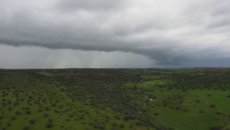 aerial footage of a dramatic storm over green hills in the countryside near azuaga, extremadura, spain. dark clouds gather in the background as the drone captures sweeping views of the lush landscape.