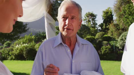 Smiling-caucasian-senior-male-wedding-officiant-standing-in-outdoor-altar,-performing-ceremony