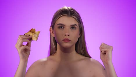 Medium-shot-of-an-attractive-young-woman-happily-biting-into-a-slice-of-delicious-vegan-pizza-while-rejoicing-and-satisfying-her-hunger-in-front-of-purple-background-in-slow-motion