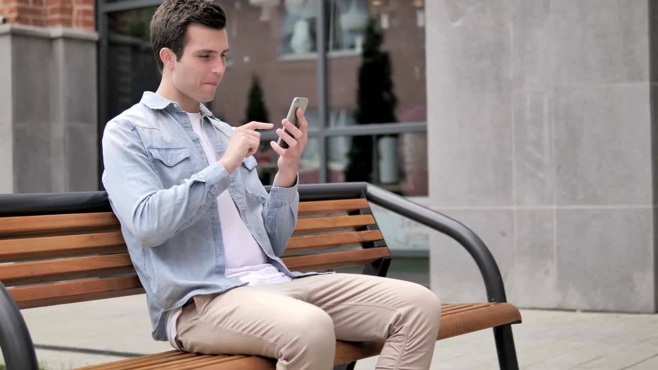 야외 젊은이가 스마트폰에서 성공을 위해 흥분하고 있습니다.