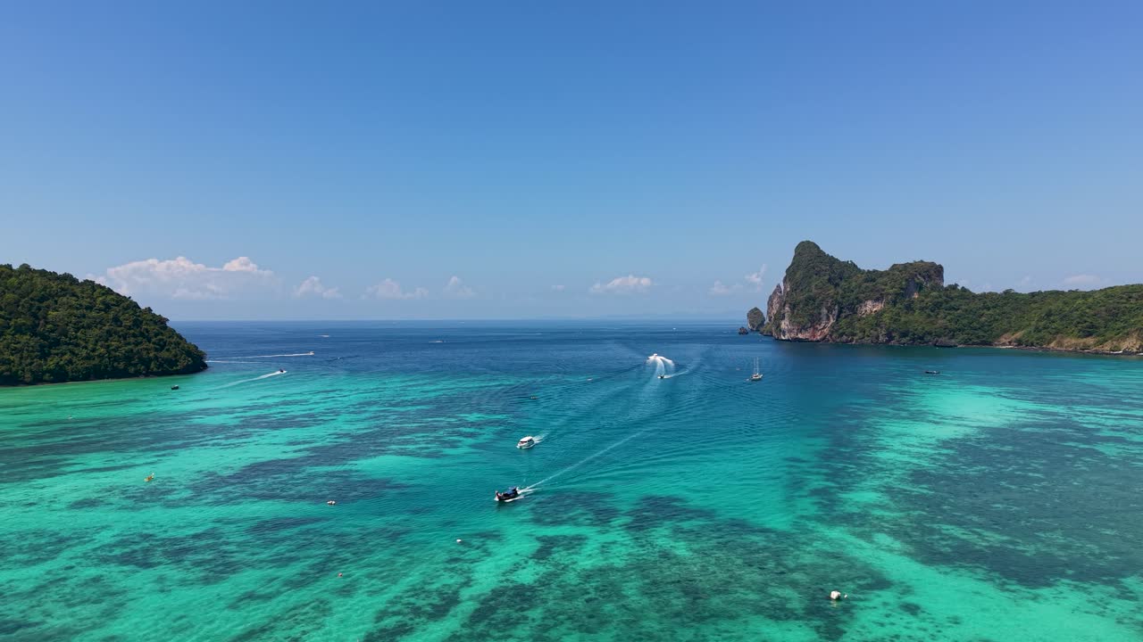 Cảnh quay trên không ghi lại những chiếc thuyền đuôi dài lướt trên mặt nước màu ngọc lam lấp lánh quanh đảo Phi Phi. Cảnh toàn cảnh tuyệt đẹp ghi lại những vách đá xanh tươi tốt dưới bầu trời xanh trong