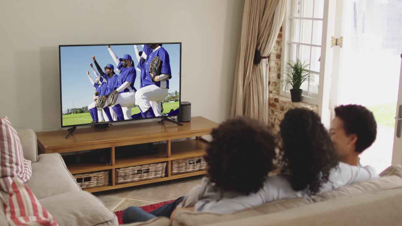 Famiglia felice seduta a casa insieme che guarda una partita di baseball in TV durante il COVID-19