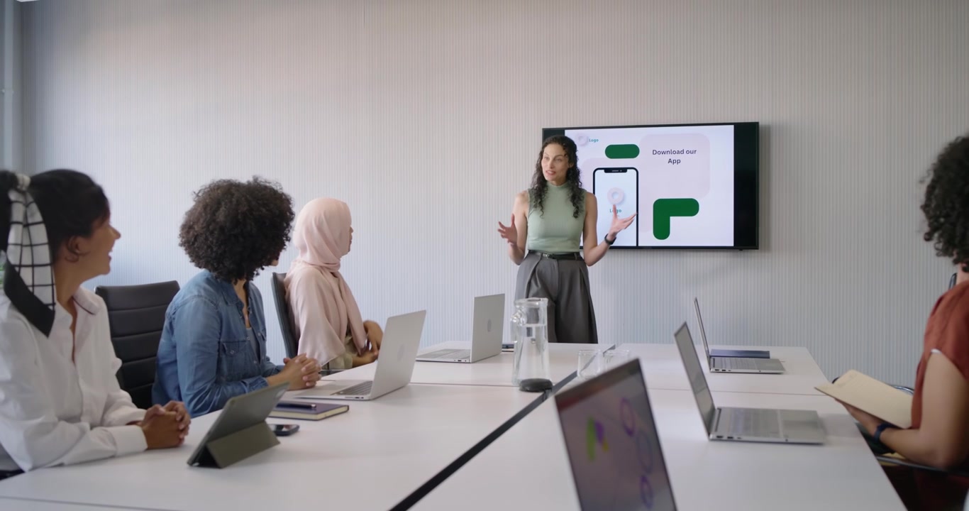 Female presenter in green pointing at screen showing app mockup sparking clapping in meeting room