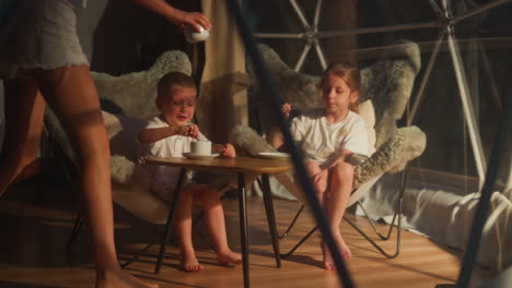 caring mother brings children ice cream in cup at glamping. woman with little son and daughter rests having dessert in tent. family camping