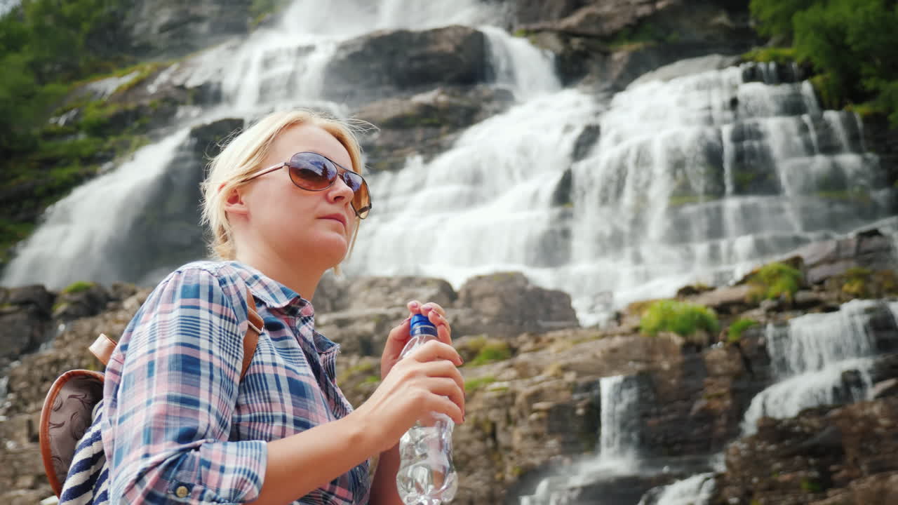 젊은 여성은 노르웨이 깨끗한 drinki에서 트윈 폭포 tvindefossen의 배경에 물을 마신다