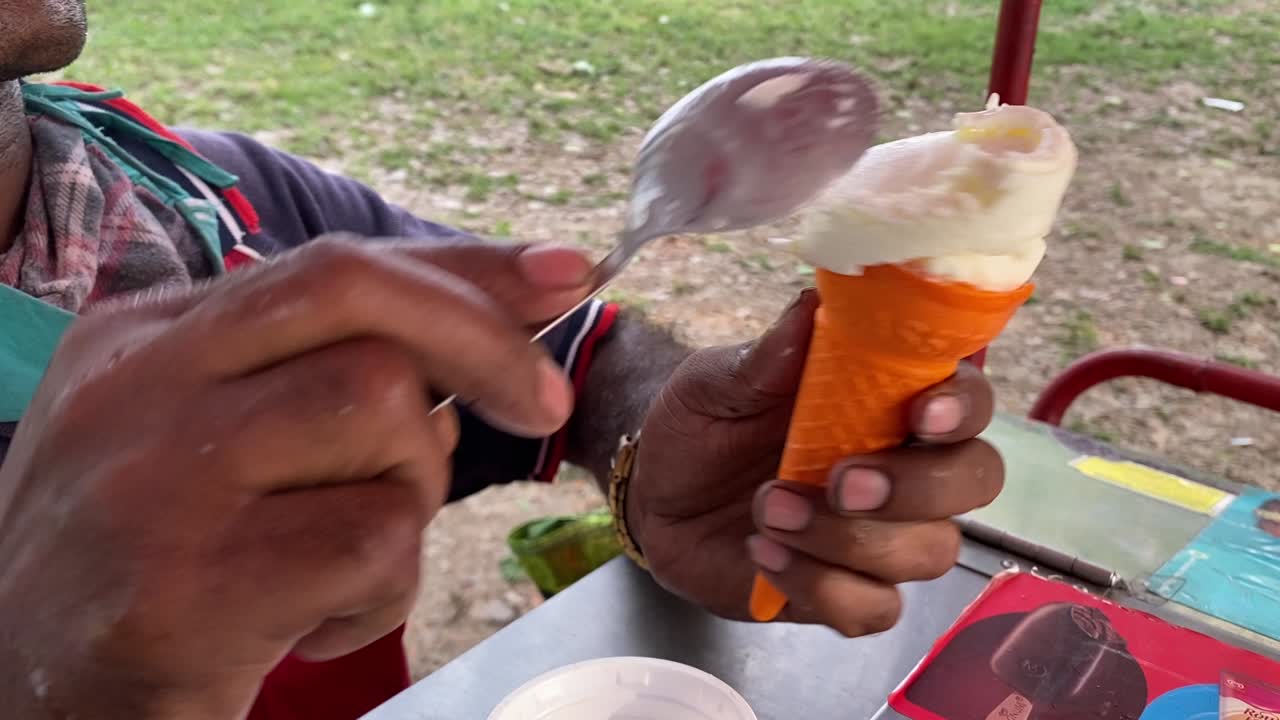 Primo piano della mano di un operatore che prepara con cura un gelato morbido alla vaniglia da un carretto Kwality Walls all'aperto