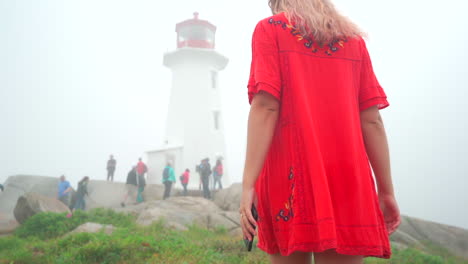 Young-woman-walking-towards-lighthouse-in-the-fog-on-an-overcast-day-in-Nova-Scotia,-Canada