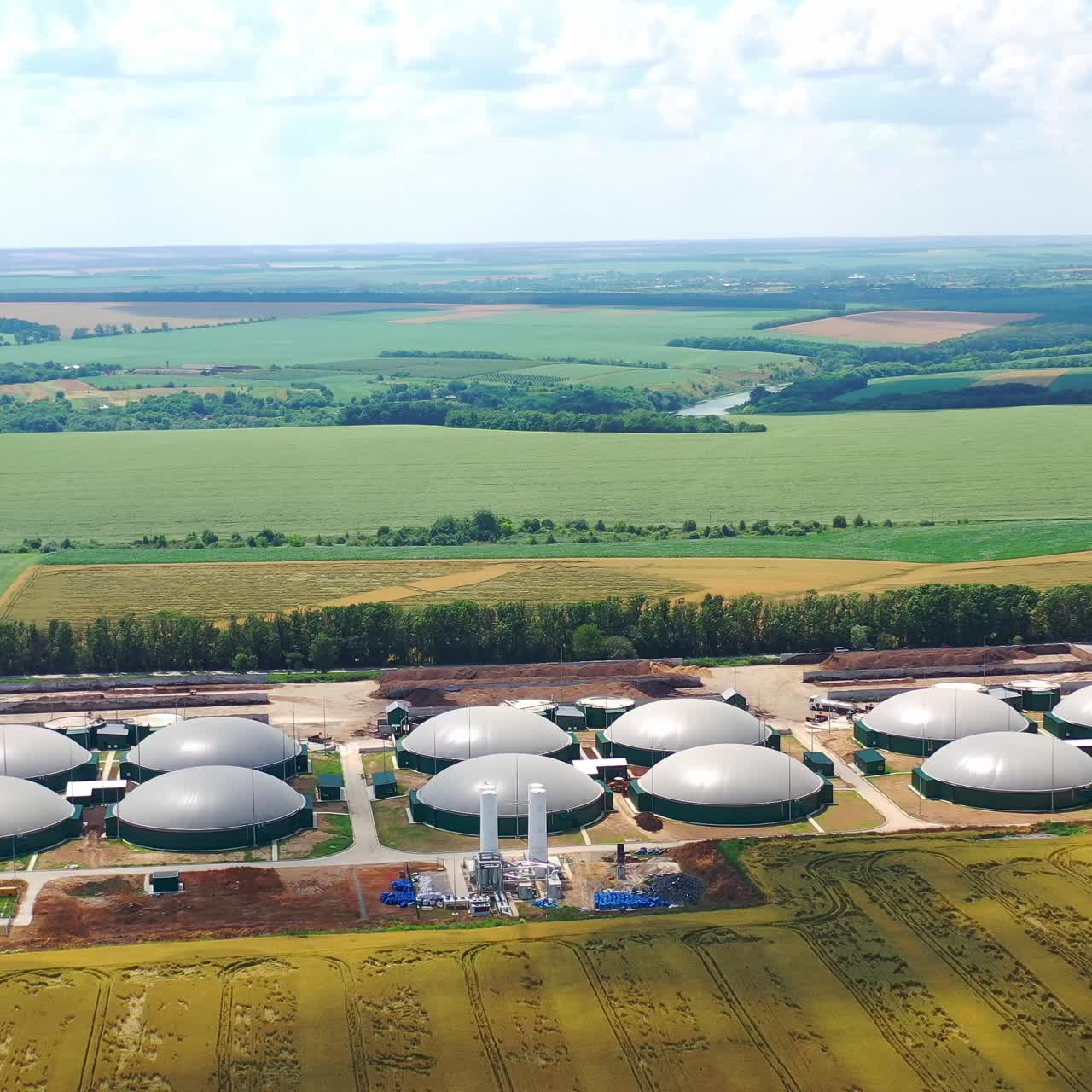 Biogas plants among green summer nature. Modern agriculture on field. Large round reservoirs for storage energy from biomass. Aerial view
