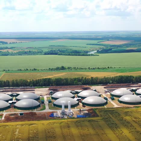 biogas plants among green summer nature. modern agriculture on field. large round reservoirs for storage energy from biomass. aerial view