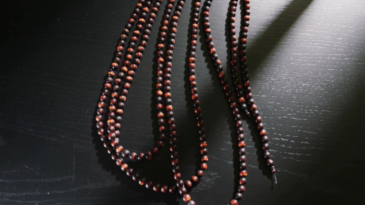 Shifting camera revealing wooden bead strands settling and exposing metal clasp on dark tabletop