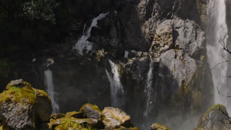 Close-up-shot-flowing-waterfall-between-rocks,-arises-from-different-springs-during-sunny-day-in-New-Zealand