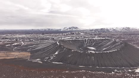 aerial view of the dark, snow-lined hverfjall crater near lake mývatn in iceland.