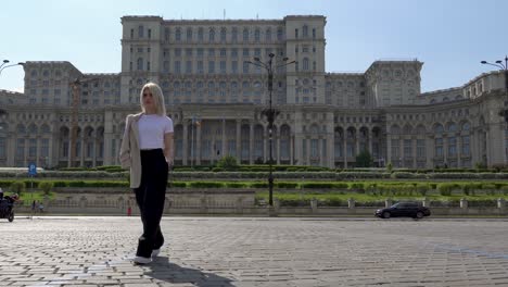 Stunning-Lady-Strolling-Towards-the-Camera-with-Palace-of-the-Parliament-in-the-Background,-Admiring-the-View,-Tourist-Destination,-Bucharest,-Romania