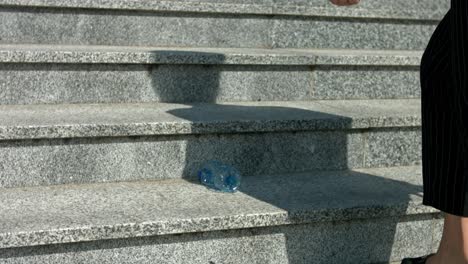 a woman picks up an empty plastic bottle from the ground to throw it in a recycling bin