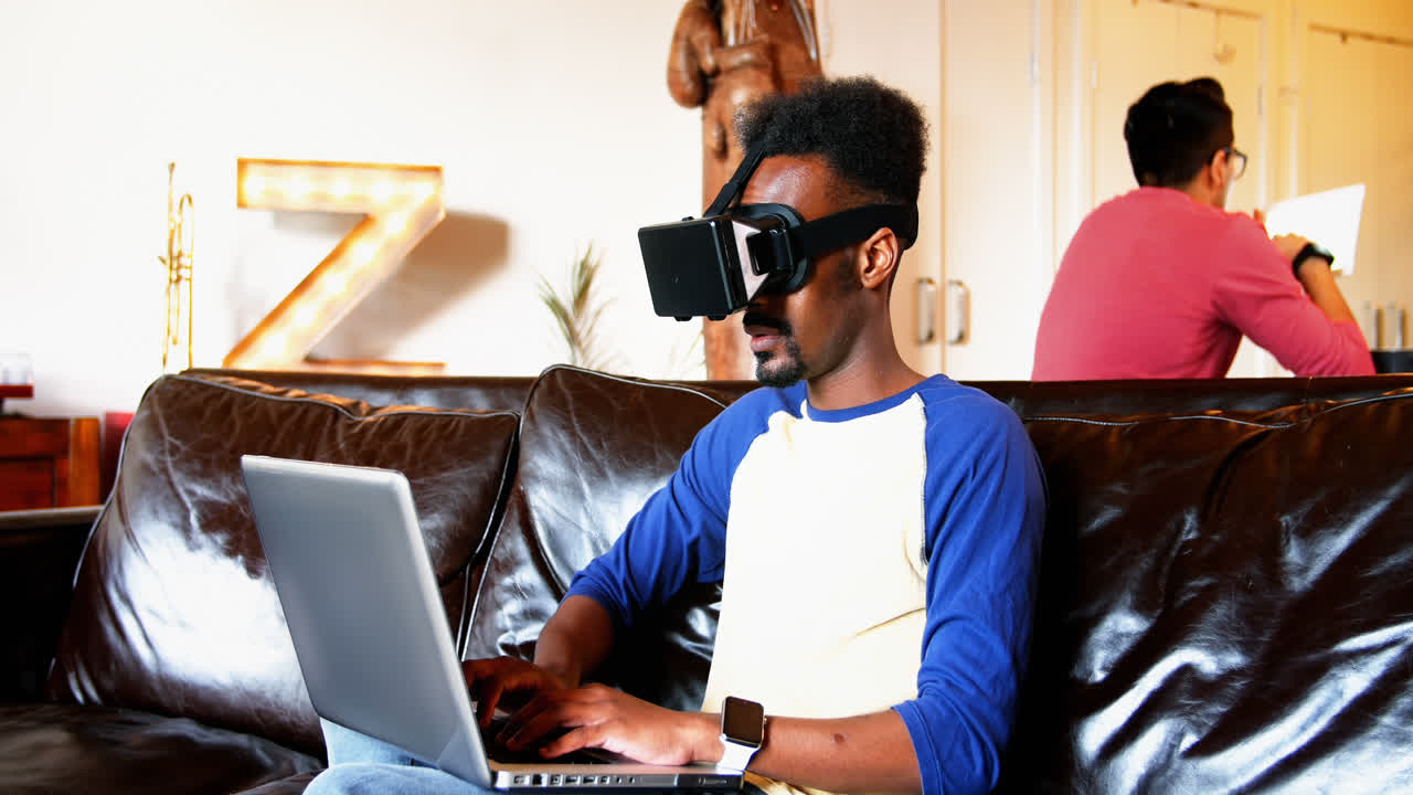 Man using virtual reality headset and laptop in living room