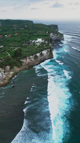 uluwatu’s limestone cliffs rise boldly from the bali coast as seen from this vertical drone view above bright blue water offering a vivid look at one of the island’s iconic seascapes.