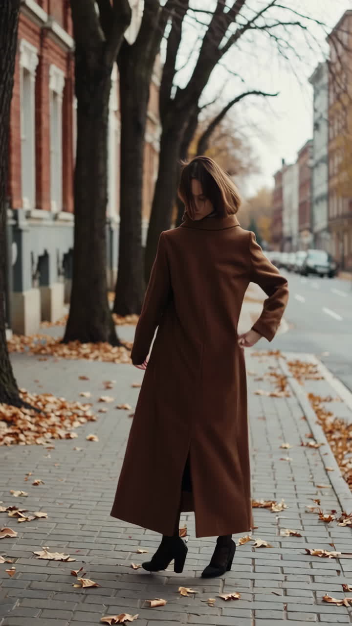 Una donna con un lungo cappotto marrone cammina per le strade autunnali della città