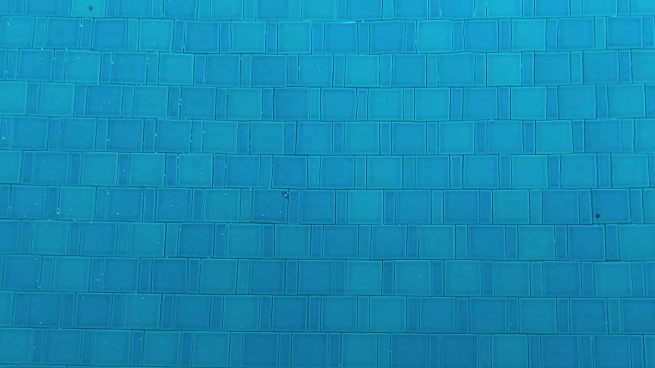 Scatto subacqueo che mostra le piastrelle blu di una piscina con acqua limpida, evidenziando l'atmosfera rinfrescante e pulita.