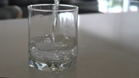 Slow-motion-wide-shot-of-water-being-poured-into-a-clear-glass-with-bubbles-rising-to-surface