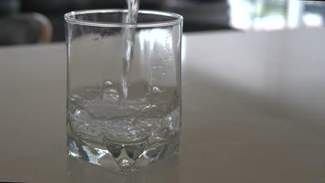 slow motion wide shot of water being poured into a clear glass with bubbles rising to surface