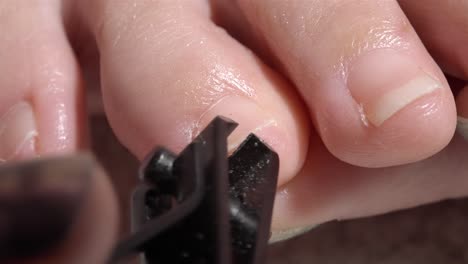 front-facing 4k shot of woman trimming small toenail corner using black clipper